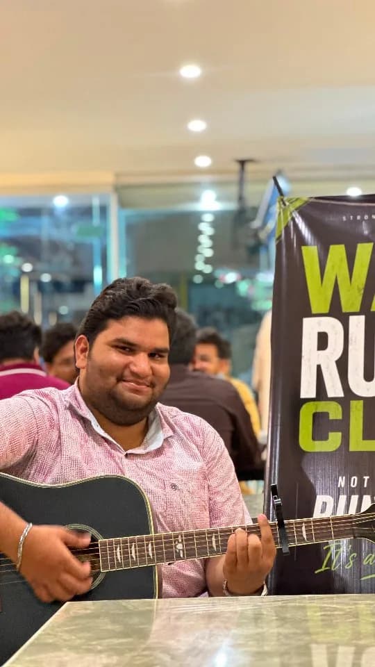 A musician playing guitar beside a Wah Run Club banner at the club’s social evening